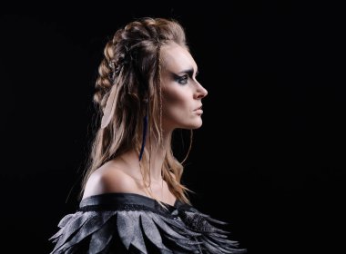 Siyah arka planda cadılar bayramı için makyaj ve kostüm giymiş güzel bir kadın. Bir gaddar ya da Valkyrie 'nin fantezi görüntüsü. Kelt mitolojisi karakteri. Kanatlar ve tüyler. Dumanlı gözler. Karnaval kızı Kara Kuş