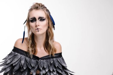 Beyaz arka planda cadılar bayramı için makyaj ve kostüm giymiş güzel bir kadın. Bir gaddar ya da Valkyrie 'nin fantezi görüntüsü. Kelt mitolojisi karakteri. Kanatlar ve tüyler. Dumanlı gözler. Karnaval kızı Kara Kuş