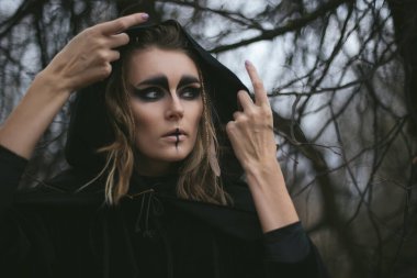 Kapüşonlu bir cadının portresi ve ormanda bir pelerin. Cadılar Bayramı mistik atmosferi. Kelt mitolojisi tanrıçası Valkyrie. Spiritüalizm büyü ayini. Maskeli balo kostümlü cadısı. Sihirli büyücülük. D