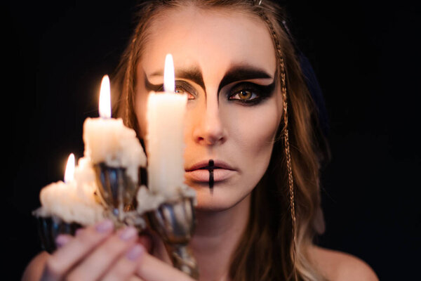 Portrait of a witch with candle. Halloween mystical atmosphere. Celtic mythology goddess Valkyrie. Spiritualism spell rite. Masquerade makeup costume. Magic witchcraft occultism. Mystic mood lifestyle