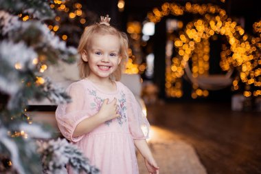 Sevimli bir kız samimi bir şekilde gülümser. Çocuk Noel 'i bekliyor. Yeni yıl için bir çocuğun portresi. Şenlikli Bokeh çelenkleri. Boşluğu kopyala