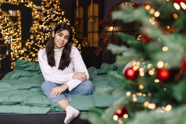 Noel ağacının yanında, yatakta süveter giyen güzel genç bir kadın.