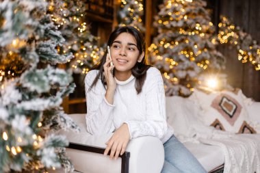 Genç kız çevrimiçi mağazadan bir Noel hediyesi alır. Noel indirimi. Mesafe alışverişi. Bir kadın elinde bir akıllı telefon tutuyor. Bayram havası, tatil beklentisi. Irk çeşitliliğini karıştır