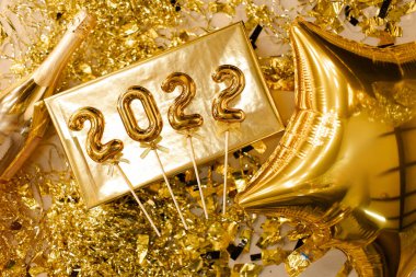Mutlu yıllar 2022 konsepti. Folyo altın numaralar 2022 üst görünüm. Şenlik dokusu. Tebrik kartı. Altın parıltılı metalik. Hediye kutusu, balon ve şampanya.