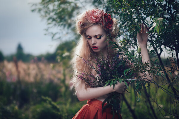 Art fashion portrait of young blond girl with flowers in hair on meadow