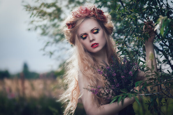 Art fashion portrait of young blond girl with flowers in hair on meadow