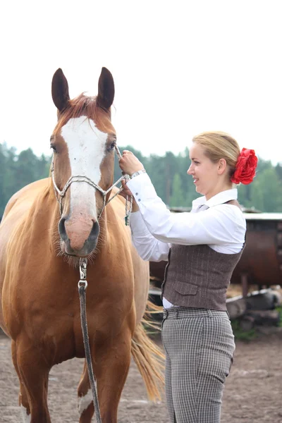 美しい若いブロンドの女性の乗馬のための馬の準備をします。 — ストック写真