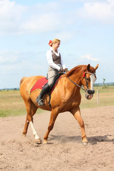 Beautiful young blonde woman riding chestnut horse — Stock Photo, Image