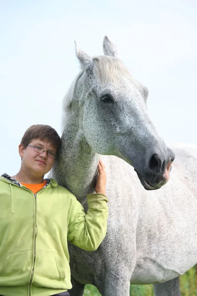 Happy teenager boy and white horse at the field — Stock Photo, Image