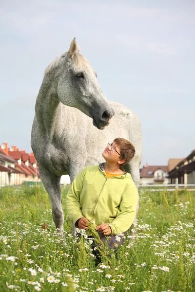 Nastolatek szczęśliwy chłopiec i biały koń w polu — Zdjęcie stockowe