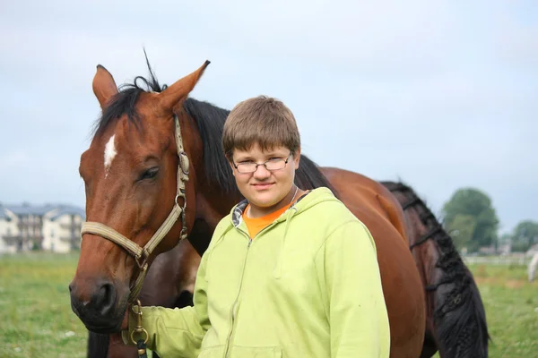 Smiling teenager boy with horses at the field — Stock Photo, Image