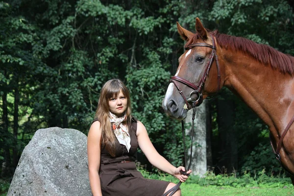 Piękna nastolatka spoczywa na skale, w parku i koń sta — Zdjęcie stockowe