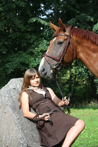 Piękna nastolatka spoczywa na skale, w parku i koń sta — Zdjęcie stockowe