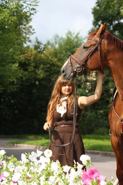 Hermosa chica en vestido y retrato de caballo cerca de la cama de flores —  Fotos de Stock