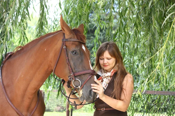 Tjej i klänning och bruna hästen stående i skogen — Stockfoto