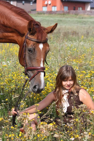 Chica sentada en el suelo y caballo castaño de pie cerca — Foto de Stock