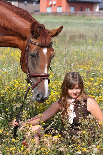 Mädchen auf dem Boden sitzend und Kastanienpferd in der Nähe — Stockfoto