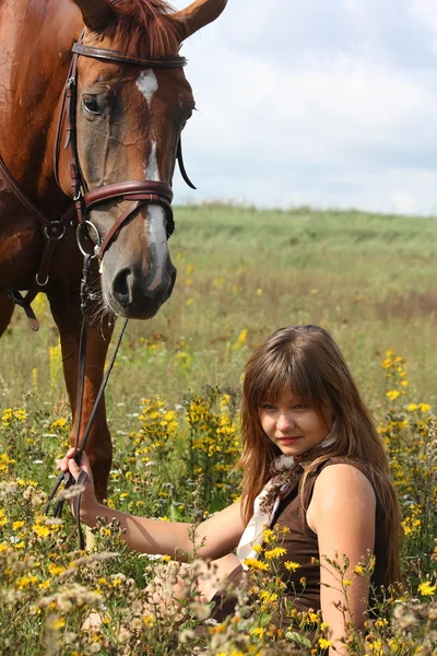 Ragazza seduta a terra e cavallo di castagno in piedi vicino — Foto Stock