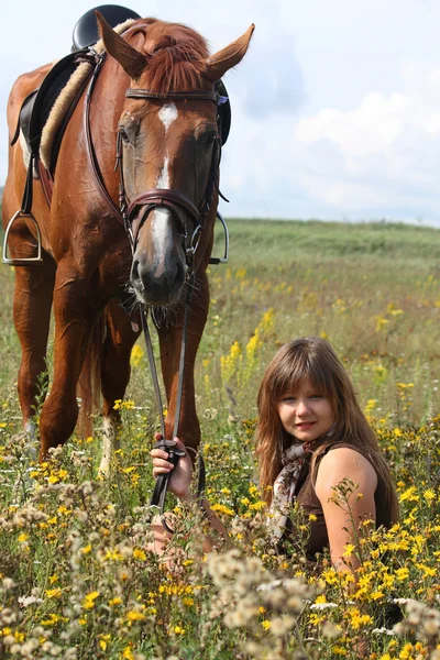 Chica sentada en el suelo y caballo castaño de pie cerca —  Fotos de Stock
