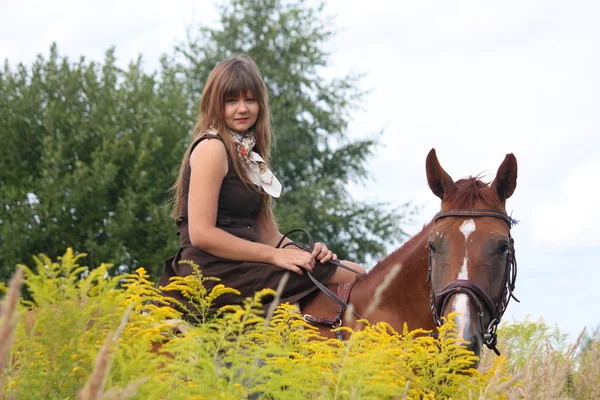 Beautiful teenager girl riding horse at the field of flowers — Stock Photo, Image