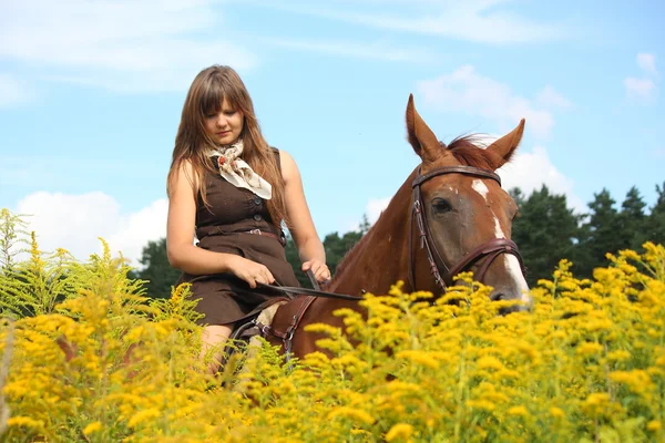 Beautiful teenager girl riding horse at the field of flowers — Stock Photo, Image