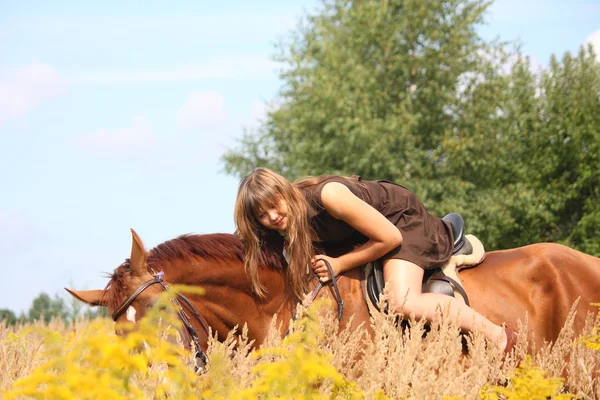 Beautiful teenager girl riding horse at the field of flowers — Stock Photo, Image