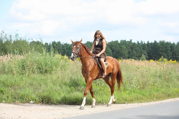 Teenage girl riding chestnut horse along the road — Stock Photo, Image