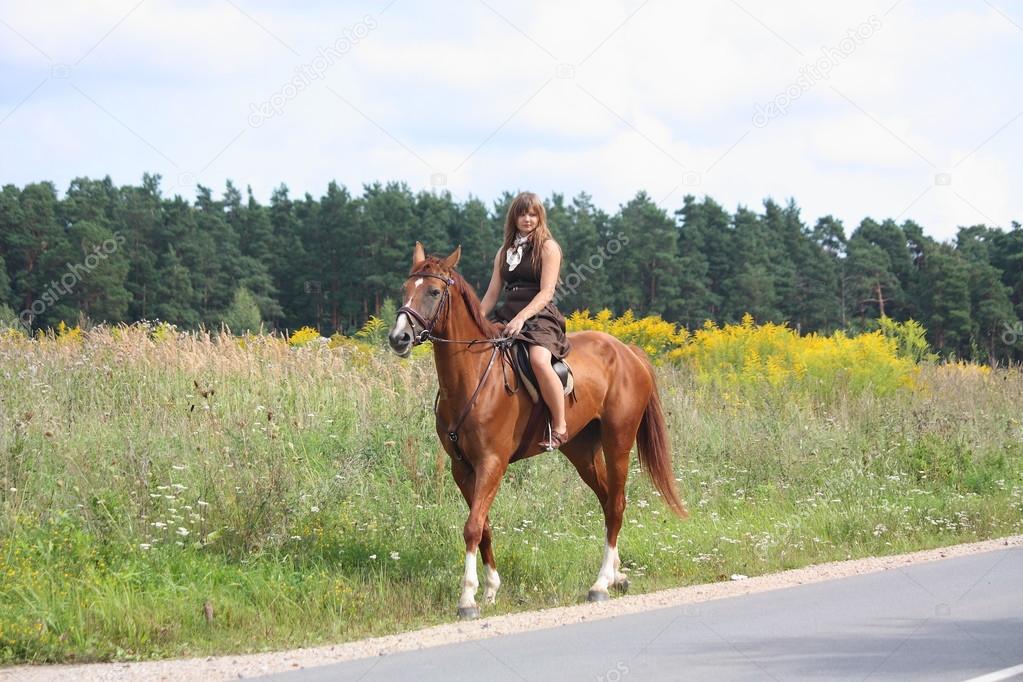 Teenage girl riding chestnut horse along the road