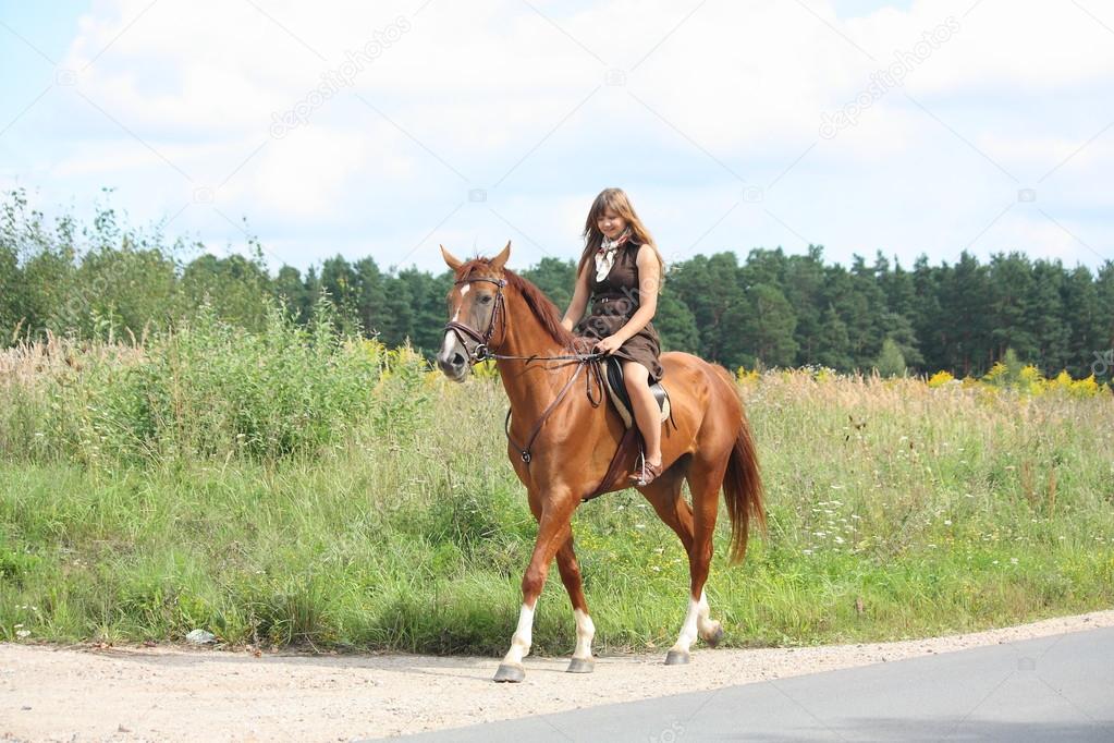 Teenage girl riding chestnut horse along the road