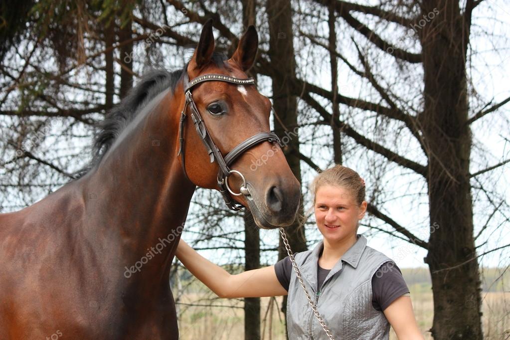 Young blonde woman and bay horse together