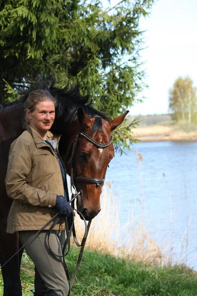 Jovem mulher e cavalo marrom juntos na costa do rio — Fotografia de Stock