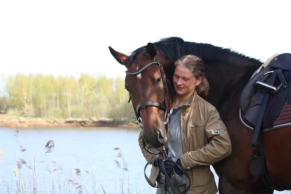 Giovane donna e cavallo marrone insieme sulla costa del fiume — Foto Stock