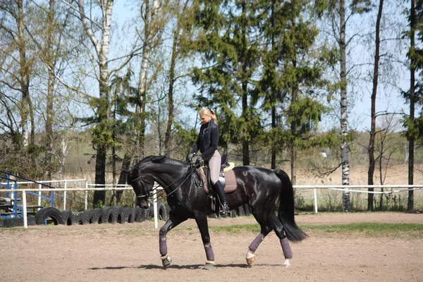 Mulher loira montando cavalo preto — Fotografia de Stock