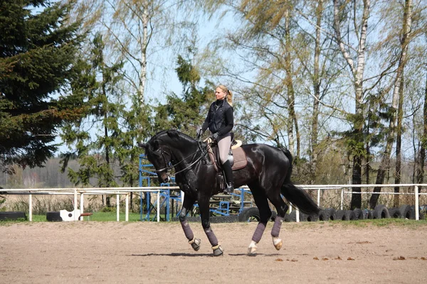 Blonde Frau reitet schwarzes Pferd — Stockfoto