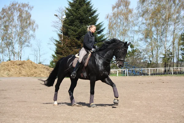 Blonde Frau reitet schwarzes Pferd — Stockfoto
