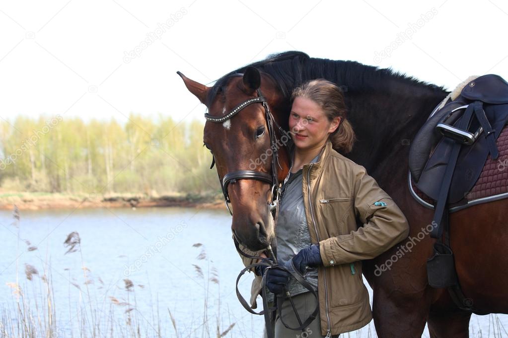 Young woman and brown horse together on the river coast