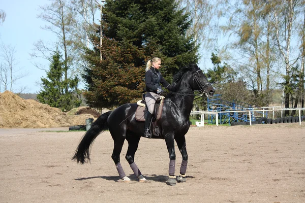 Mujer rubia montando caballo negro — Foto de Stock