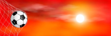 Futbol topu kale ağındadır. Günbatımının arka planında futbol topu. Kırmızı arkaplan.                                                                                                                                                          