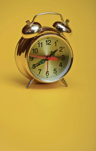 Relógio de alarme dourado em um fundo amarelo — Fotografia de Stock