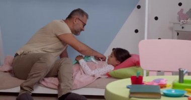 Olgun bir adam küçük torununu yatağa yatırıyor. 