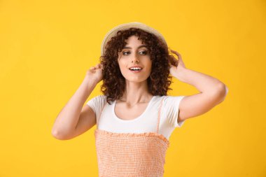 Sarı arka planda şık bir şapkası olan güzel bir kadın.