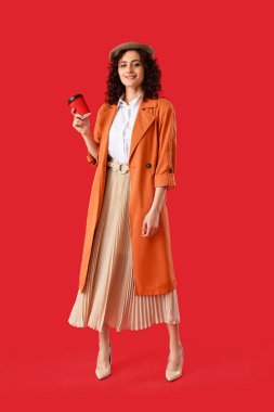 Bere şapkalı şık Parisli kadın elinde kırmızı arka planda bir fincan kahve tutuyor.