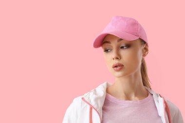 Pembe arka planda beysbol şapkalı dalgın bir kadın.