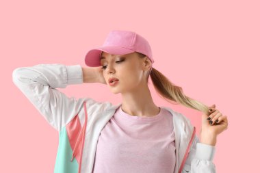 Beyzbol şapkalı genç bir kadın pembe arka plandaki saçlara dokunuyor.