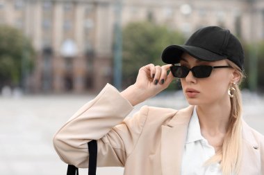 Şehir meydanında beysbol şapkası ve güneş gözlüğü takan güzel genç bir kadın.