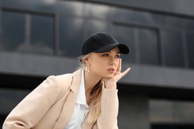 Modern bina yakınlarında beysbol şapkalı dalgın bir kadın.