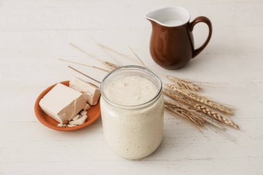 Beyaz ahşap arka planda taze ekşi mayalı cam kavanoz.