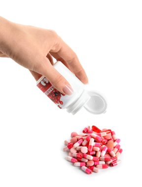 Şişeli bir kadın eli ve beyaz arka planda bir yığın yabanmersini hapı.