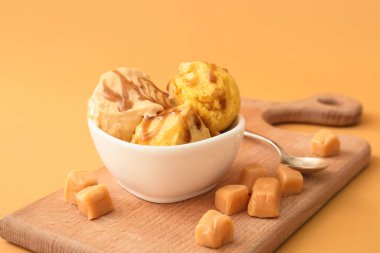 Renkli arkaplanda karamel olan lezzetli dondurma toplarıyla dolu bir kase.