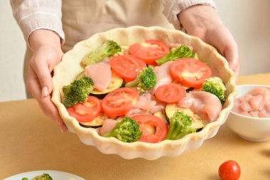 Mutfak masasında sebzeli tavuk turtası tutan bir kadın.